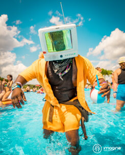 Man with a TV head and orange jacket dancing in a pool at Imagine Music Festival 2023