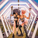 Two women with staffs and black boots standing in an LED art exhibit at Imagine Music Festival 2023