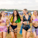 Four white women smiling and laughing together in festival outfits