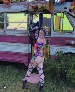Girl dressed in colorful leg wraps and two-piece outfit spinning a flowstar in front of a bus