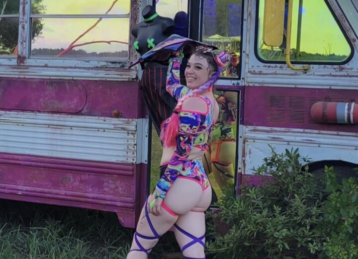 Girl dressed in colorful leg wraps and two-piece outfit spinning a flowstar in front of a bus