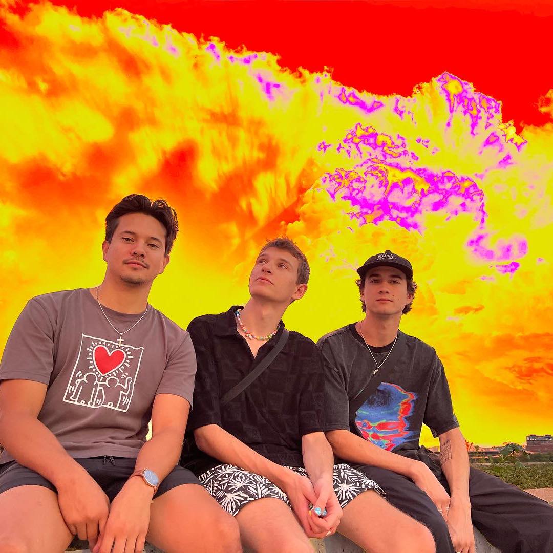 Levity press shot: the EDM trio sitting on a bench with a psychedelic sky
