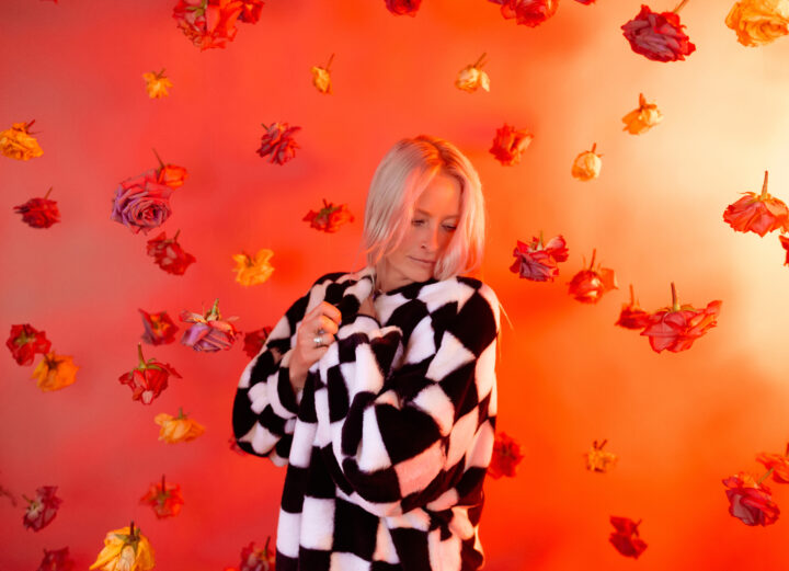 Maddy O'Neal wearing a checkered jacket in front of an orange screen